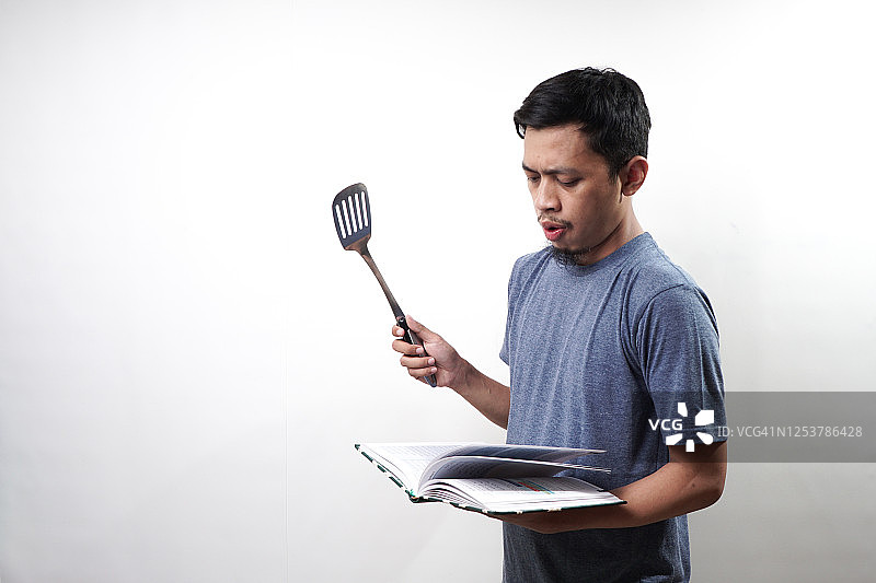 亚洲男人手持锅铲和食谱图片素材