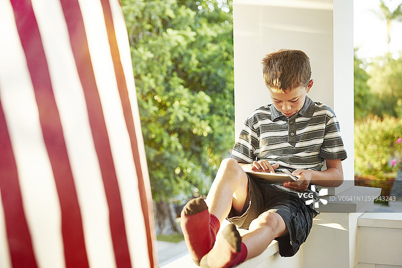 男孩在阳光明媚的门廊上看书图片素材