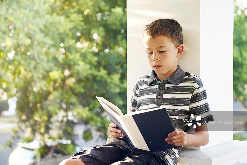 男孩在阳光明媚的门廊上看书图片素材