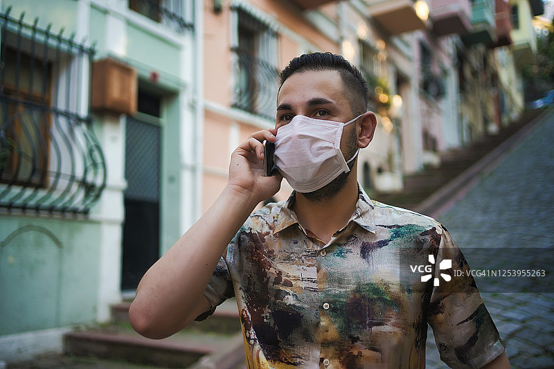 在伊斯坦布尔巴拉特区彩色房屋附近使用手机的戴防护面具的男人图片素材