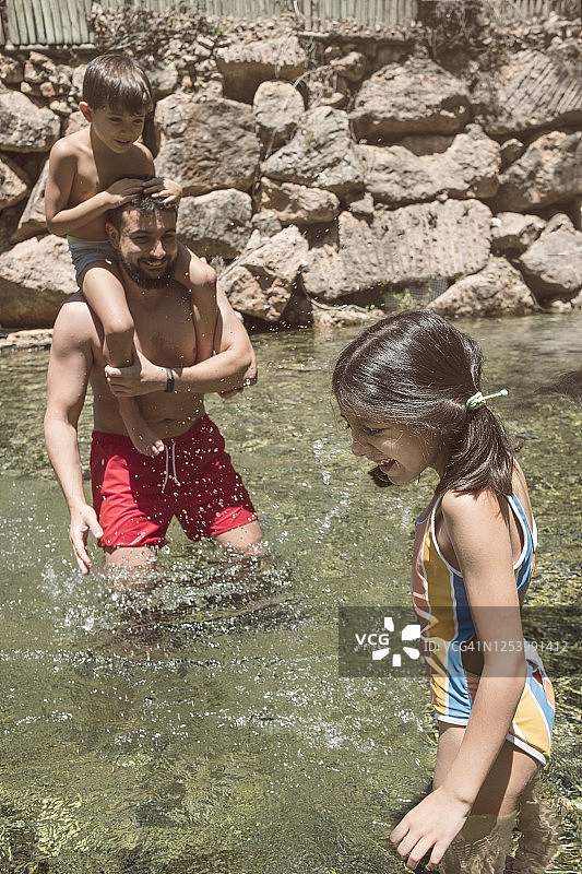 父亲和儿子在河里玩耍，儿子坐在父亲的肩膀上，女儿也在图片素材