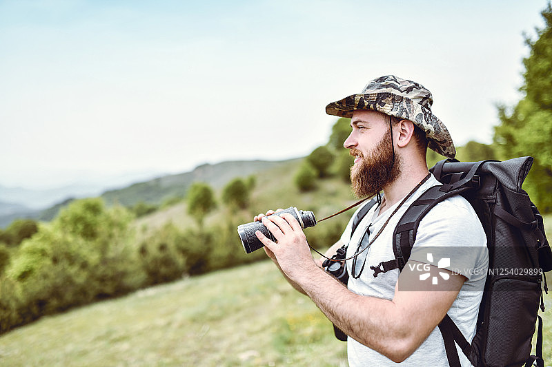 用双筒望远镜从山顶看山谷的英俊男徒步旅行者图片素材