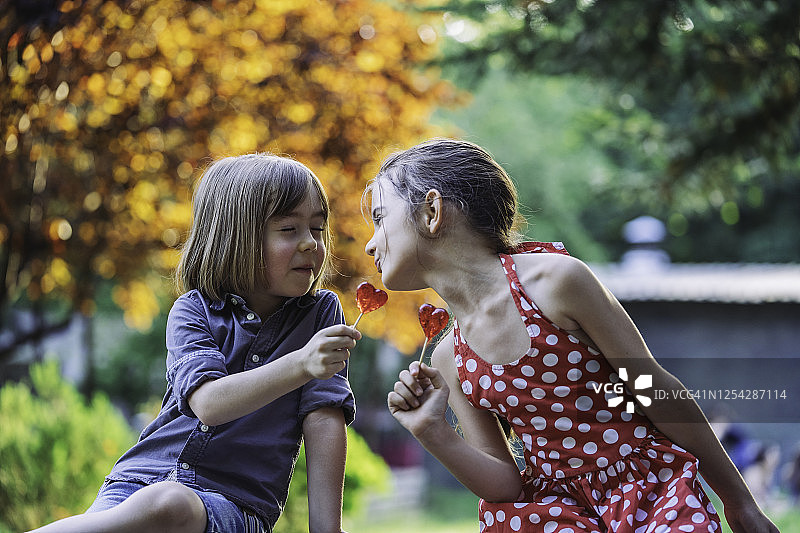 两个孩子在说话和吃棒棒糖。孩子们在公园里玩得很开心。图片素材