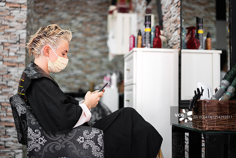 年轻的白人女性在理发店戴着防护口罩发短信图片素材