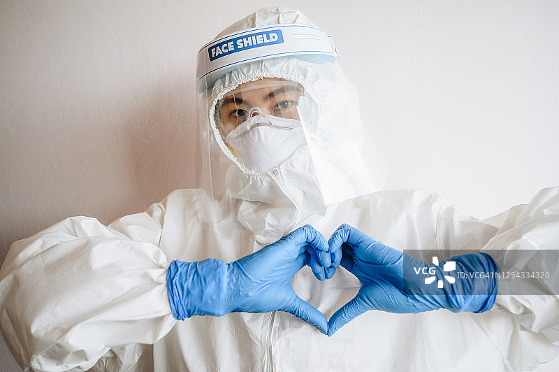 医护人员在胸前用手指做出爱心手势，表达爱意，同时穿着个人防护装备在医院工作。图片素材