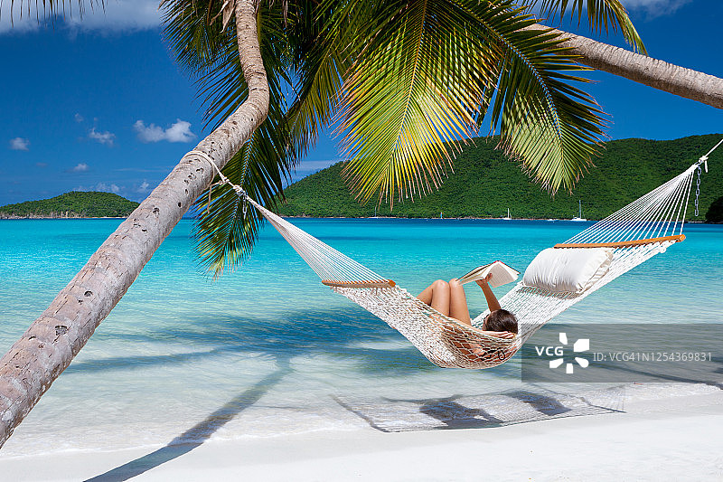 在热带海滩吊床上阅读和放松的女人图片素材