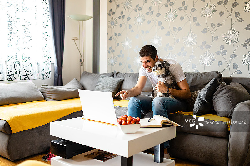 快乐的年轻男人通过视频电话向朋友介绍他的狗图片素材