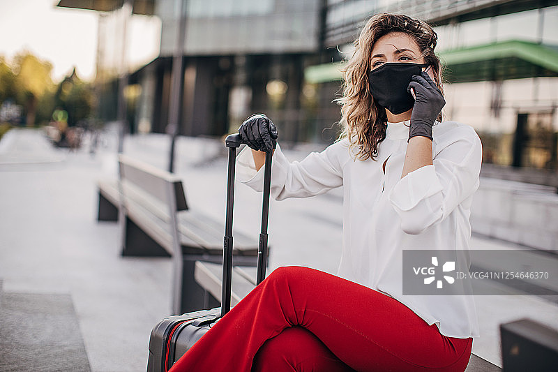 戴防护口罩和手套的年轻女商人在城市中使用智能手机图片素材