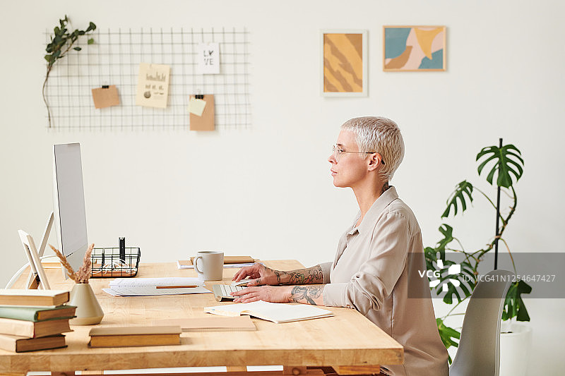 专注的中年商业女士坐在桌旁，检查电脑上的文件图片素材