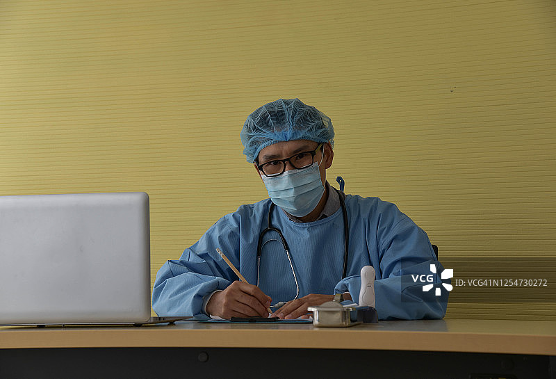 亚洲医生穿着手术服坐在医院病房的工作台旁图片素材