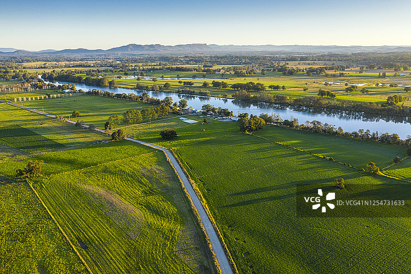 乡村公路旁的农田：日落时分的绿色田野、河流和山脉图片素材