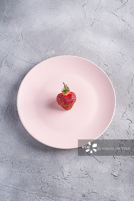粉红色盘子里的一个新鲜成熟的草莓，灰色石材背景上的夏季维生素浆果，顶视图图片素材