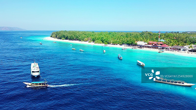 停靠在翠绿岛屿和白色沙滩岸边的船只，周围是碧蓝的海水图片素材