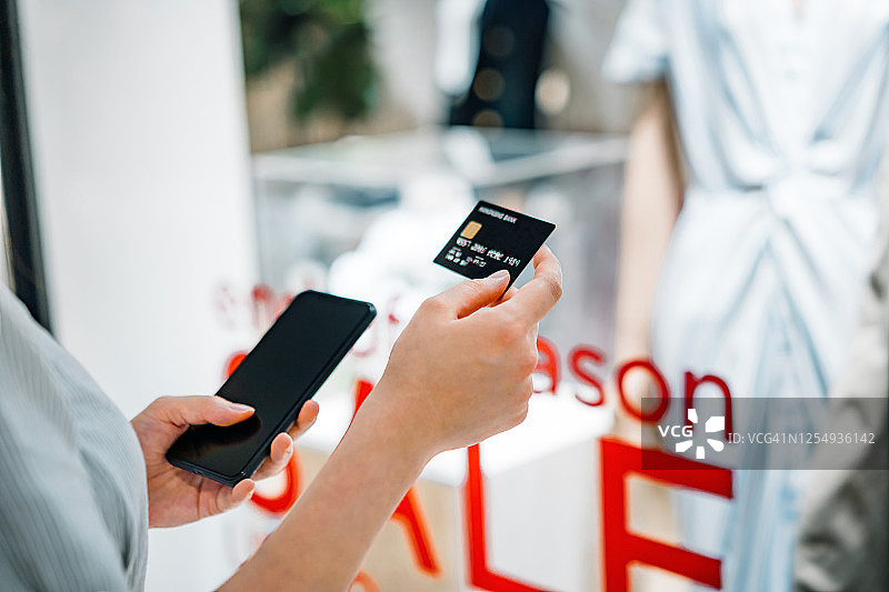 亚洲女性在服装店使用信用卡和智能手机购物图片素材