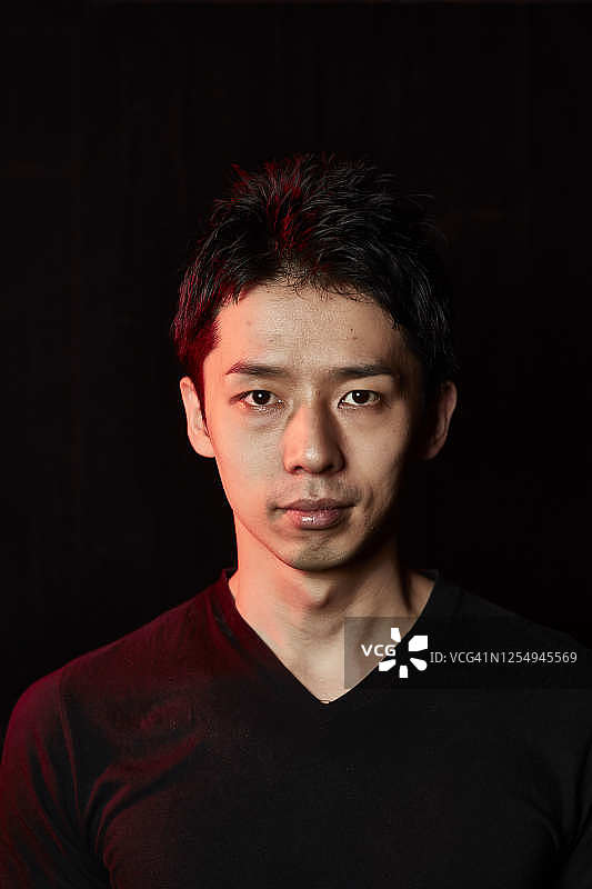橙色聚光灯照亮黑色背景下的亚洲男人图片素材