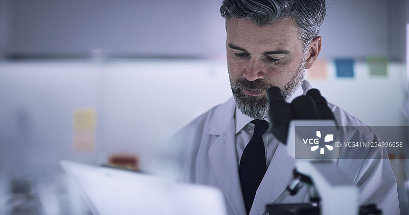 处理医疗样本：男子使用显微镜观察玻璃器皿图片素材