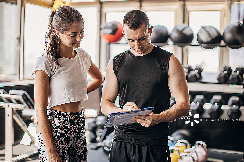 年轻健壮的女人和私人教练制定健身计划图片素材