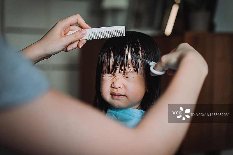 年轻的亚洲母亲在家为女儿剪头发的截取图图片素材