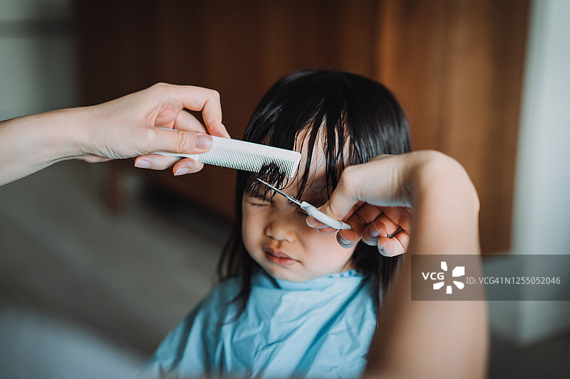 年轻的亚洲母亲在家为女儿剪头发的截取图图片素材