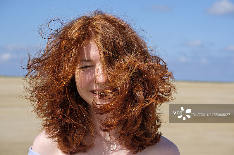 阳光明媚的日子里，闭着眼睛站在海滩上的红发少女特写图片素材