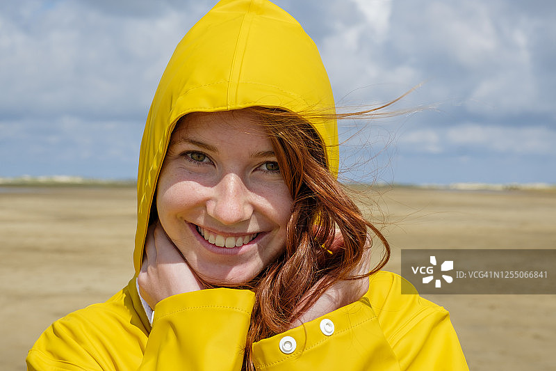 阳光明媚的日子，海滩上穿着黄色雨衣的红发少女特写图片素材