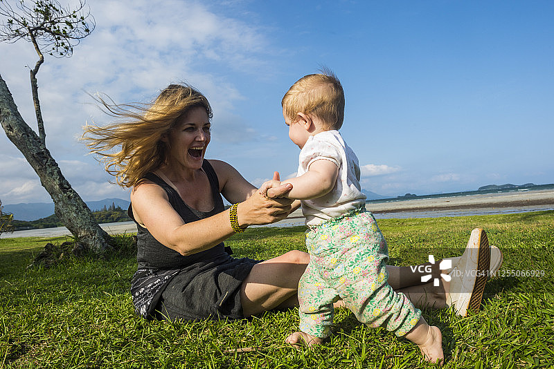 快乐的妈妈坐在草地上和蹒跚学步的女儿玩耍（新喀里多尼亚，努美阿）图片素材