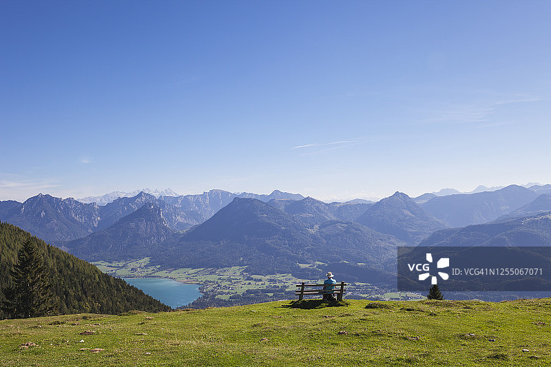 老年男性徒步旅行者坐在长椅上欣赏达赫施泰因山图片素材