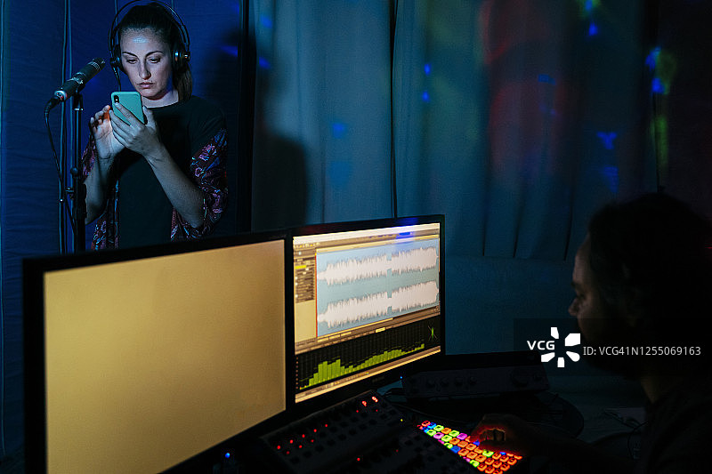 在家录音棚里使用智能手机唱歌的女人，男人使用电脑图片素材