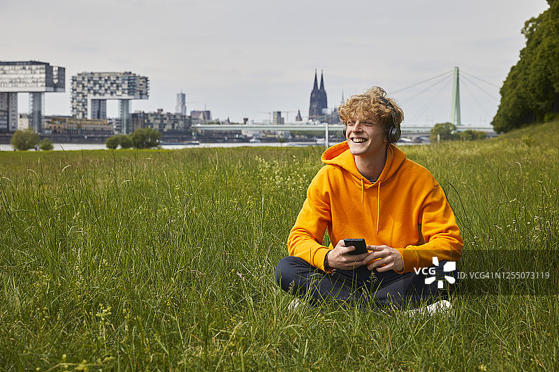 快乐的年轻人在德国科隆的草地上戴着耳机听音乐图片素材