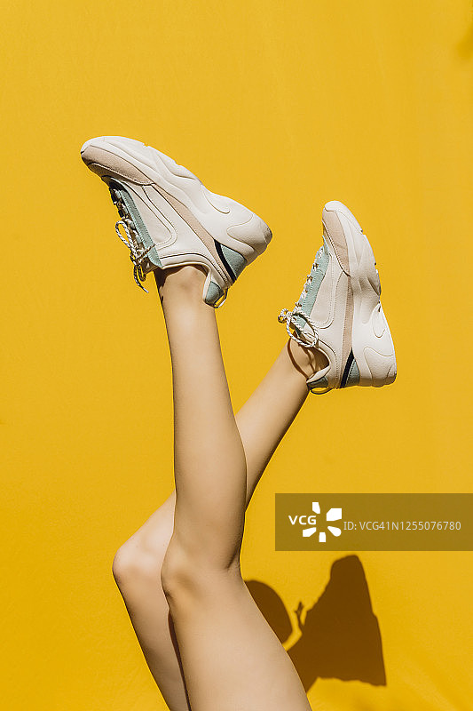 阳光明媚的日子里，黄色墙壁前的女士运动鞋图片素材