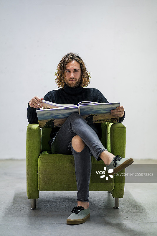 表情严肃的男人坐在扶手椅上看书图片素材