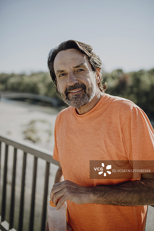 微笑的成熟男人拿着水瓶站在公园的晴空下图片素材