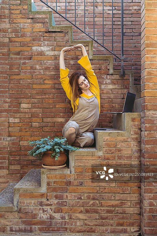 年轻女子坐在台阶上，用笔记本电脑和智能手机伸展手臂图片素材