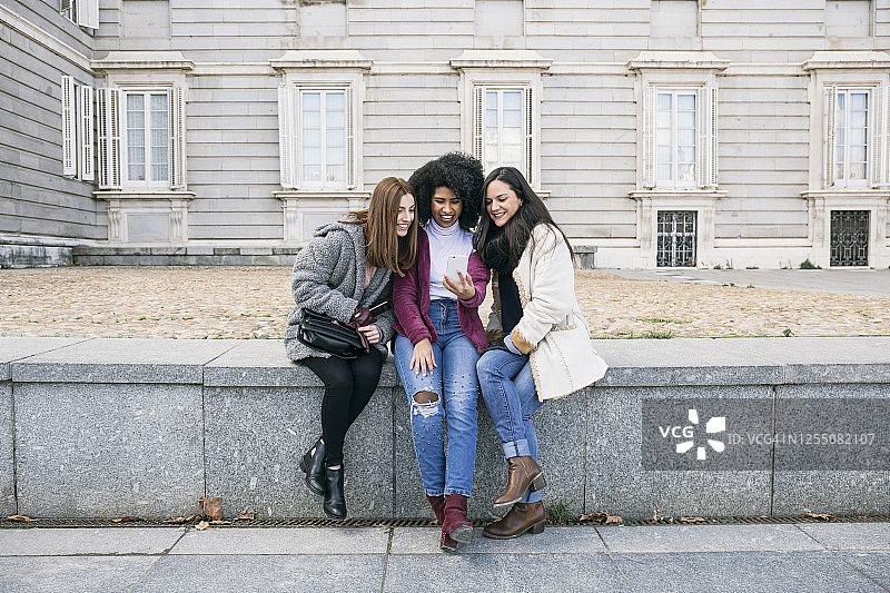 女性朋友坐在马德里皇宫的 retaining wall上使用智能手机图片素材
