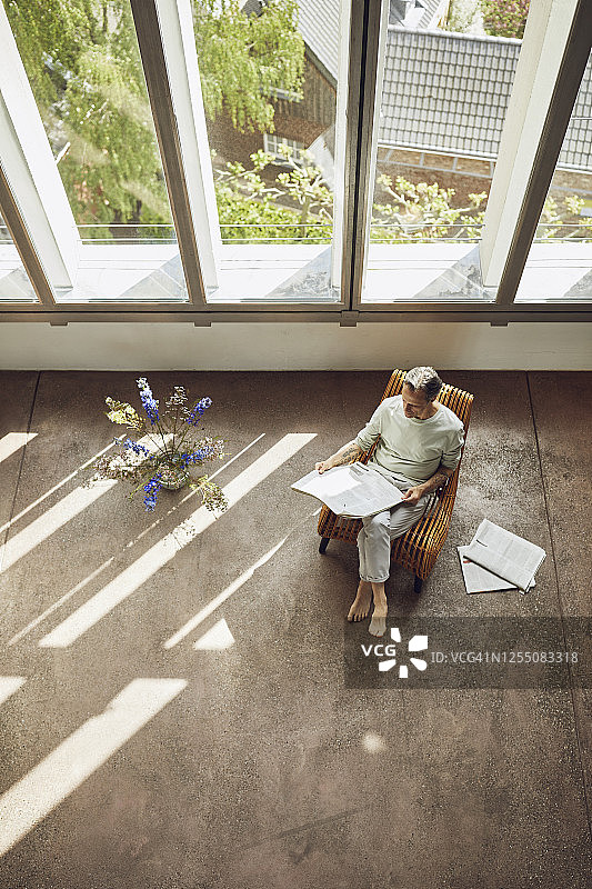 年长的男人坐在阁楼公寓的椅子上看报纸图片素材