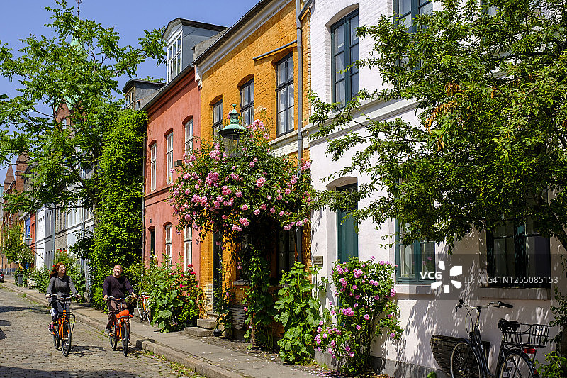 丹麦哥本哈根男女骑自行车穿过历史悠久的尼布德区街道图片素材
