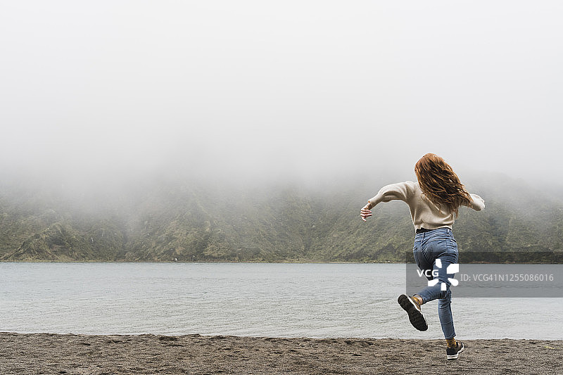 女探险家在葡萄牙亚速尔群岛圣米格尔岛的湖岸边奔跑图片素材