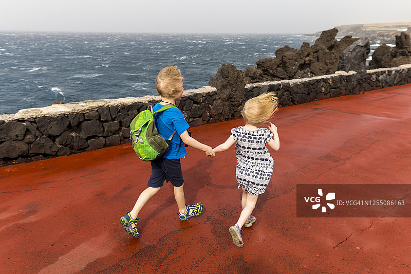西班牙特内里费岛科斯塔阿德赫海边码头上手牵着手奔跑的兄弟姐妹高角度视图图片素材