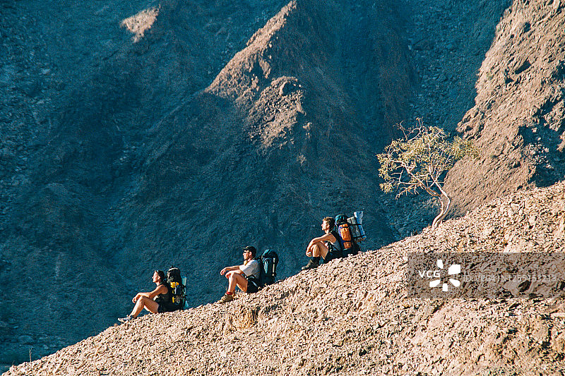 三名徒步旅行者坐在山区干旱地区的山脊上图片素材