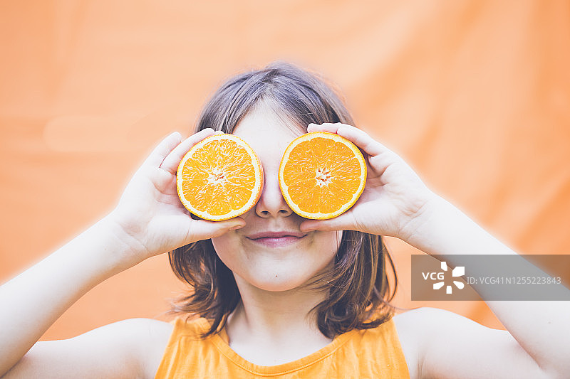 长发男孩手持半个橙子遮眼肖像图片素材