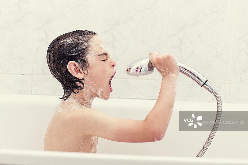 男孩坐在浴缸里，对着花洒唱歌图片素材