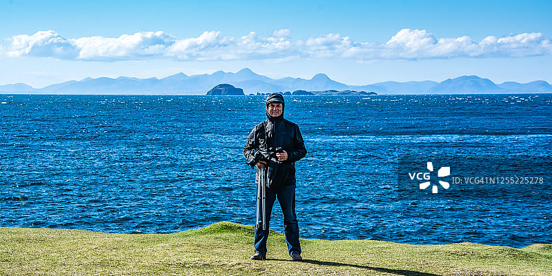站在英国苏格兰斯凯岛海岸，手持相机和三脚架的男人图片素材