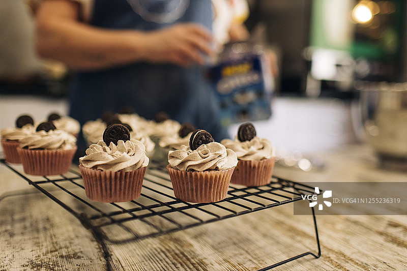 商店中，架子上纸杯蛋糕与背景中女性烘焙师的特写图片素材