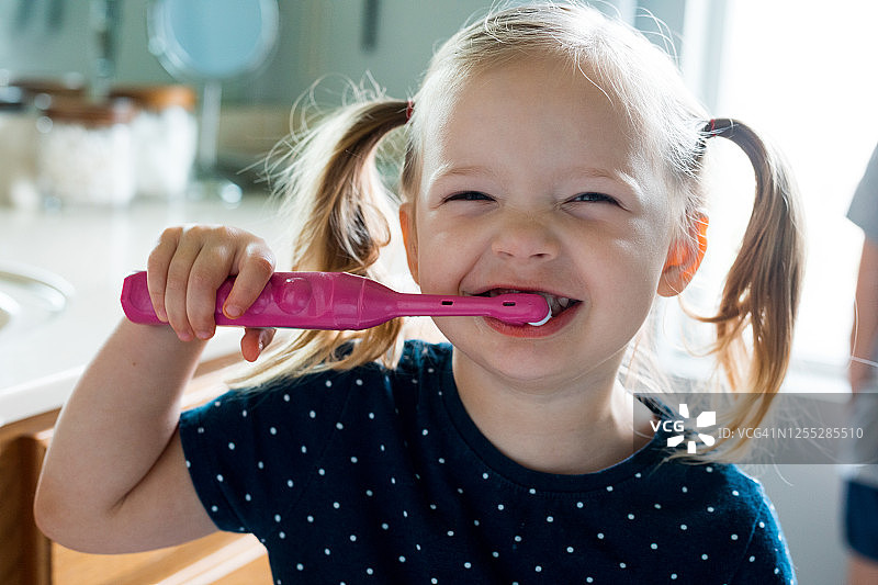 在家中浴室，幼儿女孩用电动牙刷刷牙图片素材