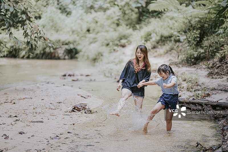 一位亚洲华人女性在河边与女儿玩耍，戏水踢水图片素材