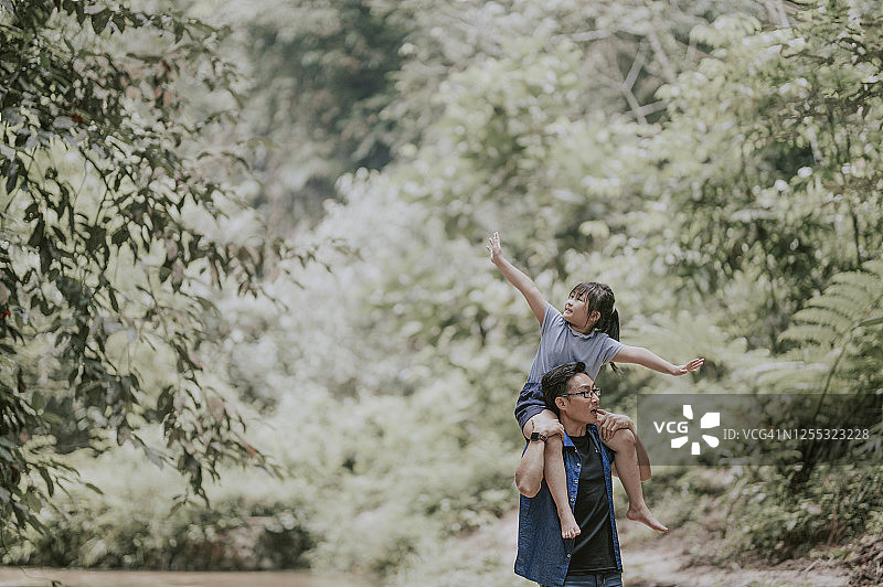 亚洲父亲在丛林中肩扛女儿享受亲子时光图片素材