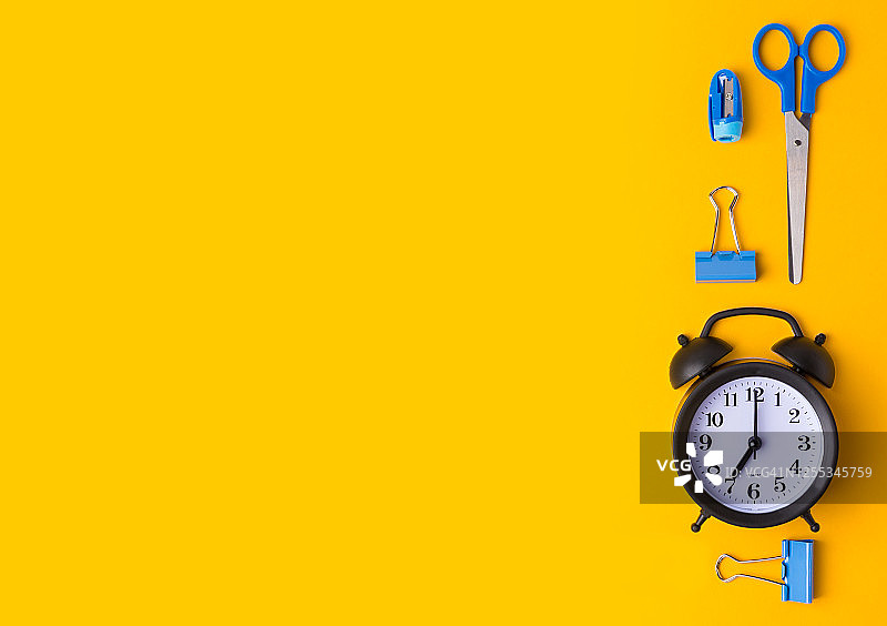 黄色背景上的闹钟和学习用品俯视图。返校概念。复制空间。图片素材