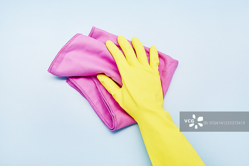 戴黄色手套的手在蓝色背景上拿着清洁布，房屋清洁图片素材