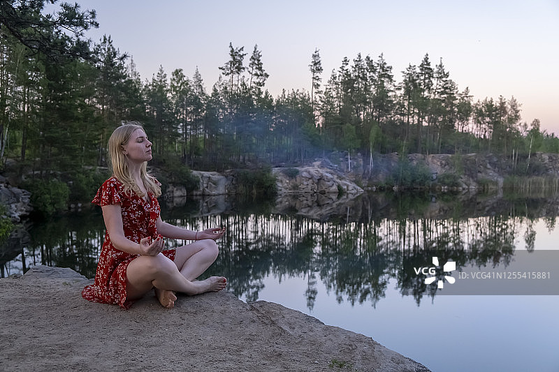 日落时分，红裙金发女子在松树林花岗岩采石场悬崖边冥想，与自然融为一体图片素材