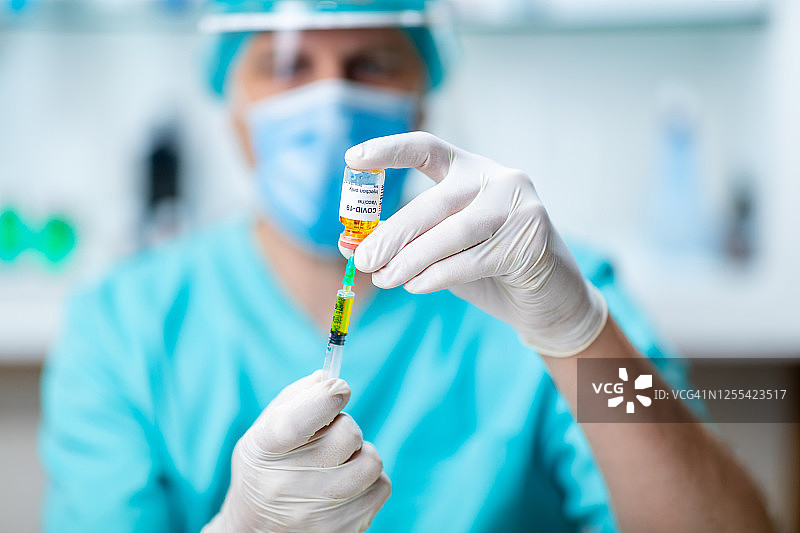 医生戴着外科手套从小瓶中抽取COVID-19疫苗图片素材